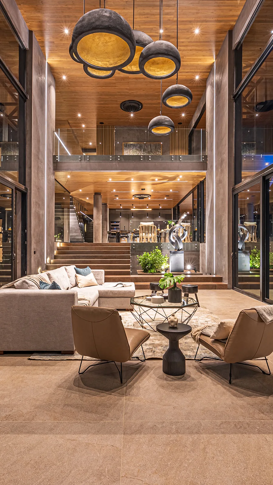 Double-height Alianz living room at night, sculptural pendant lights glowing warmly over the lounge