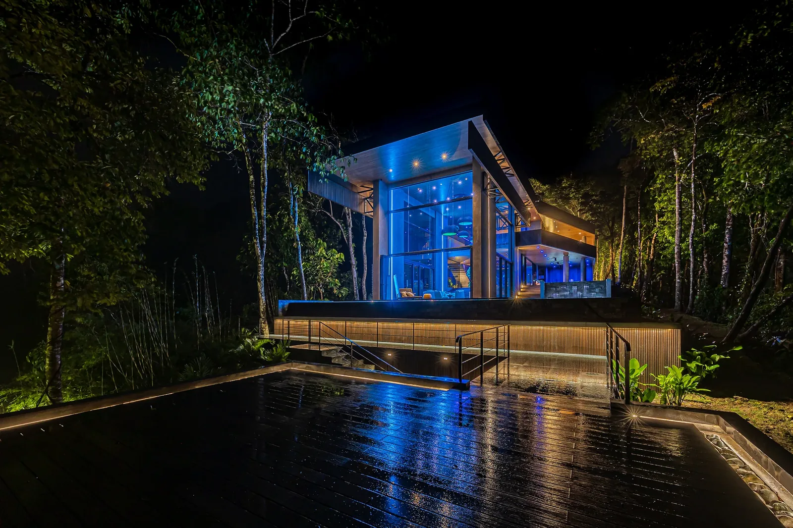 Alianz residence at night in the rainforest, glass facade glowing while the pool deck reflects the illuminated interior