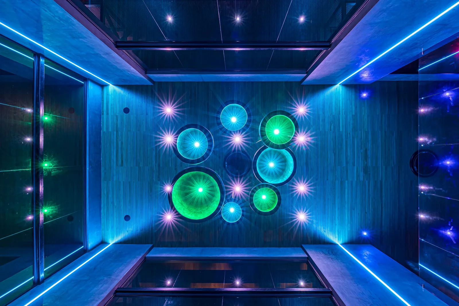 Sculptural ceiling with recessed circular speakers and turquoise accent lighting in an Alianz residence
