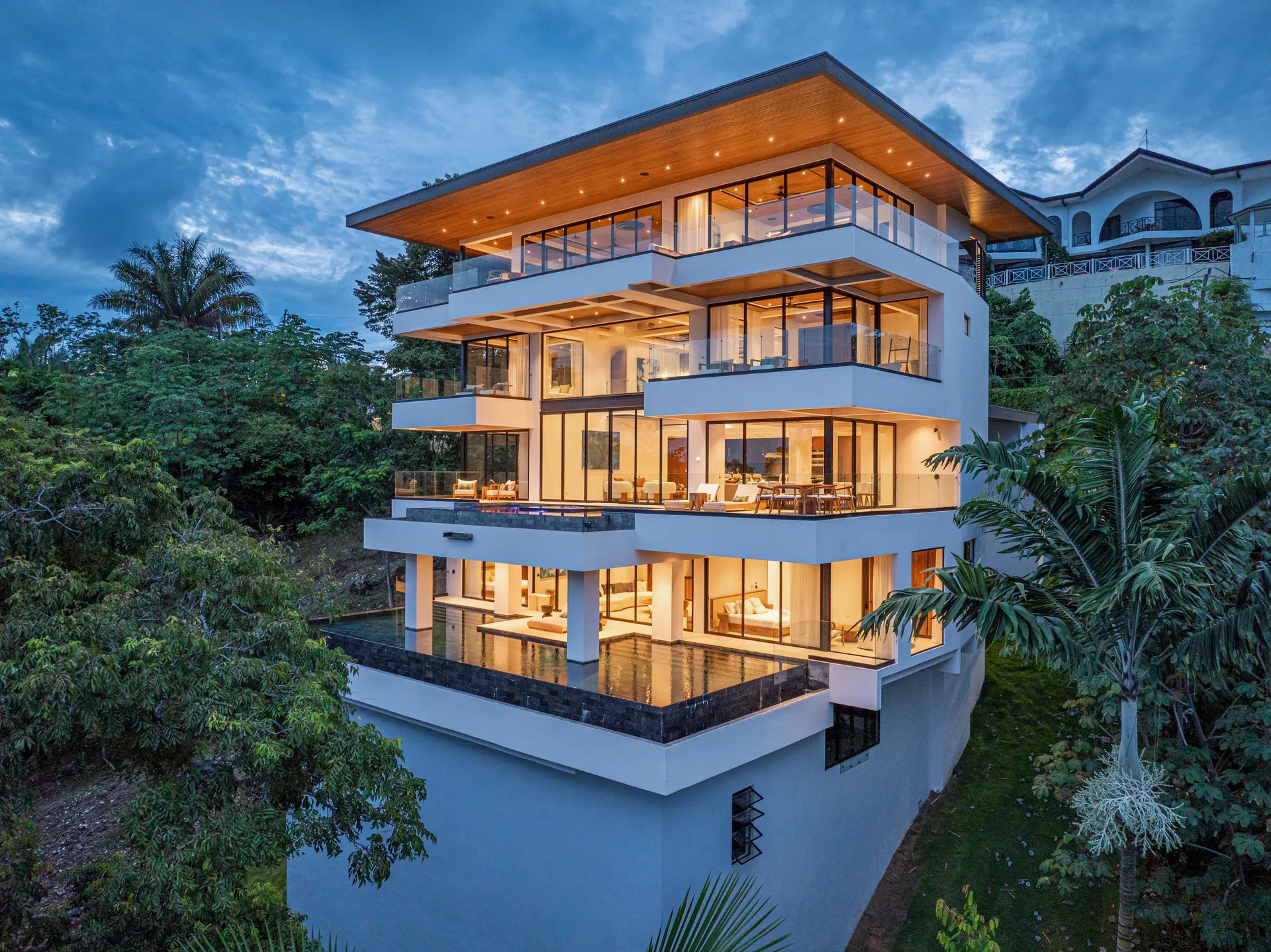 Multi-level Alianz residence glowing at dusk on a rainforest hillside