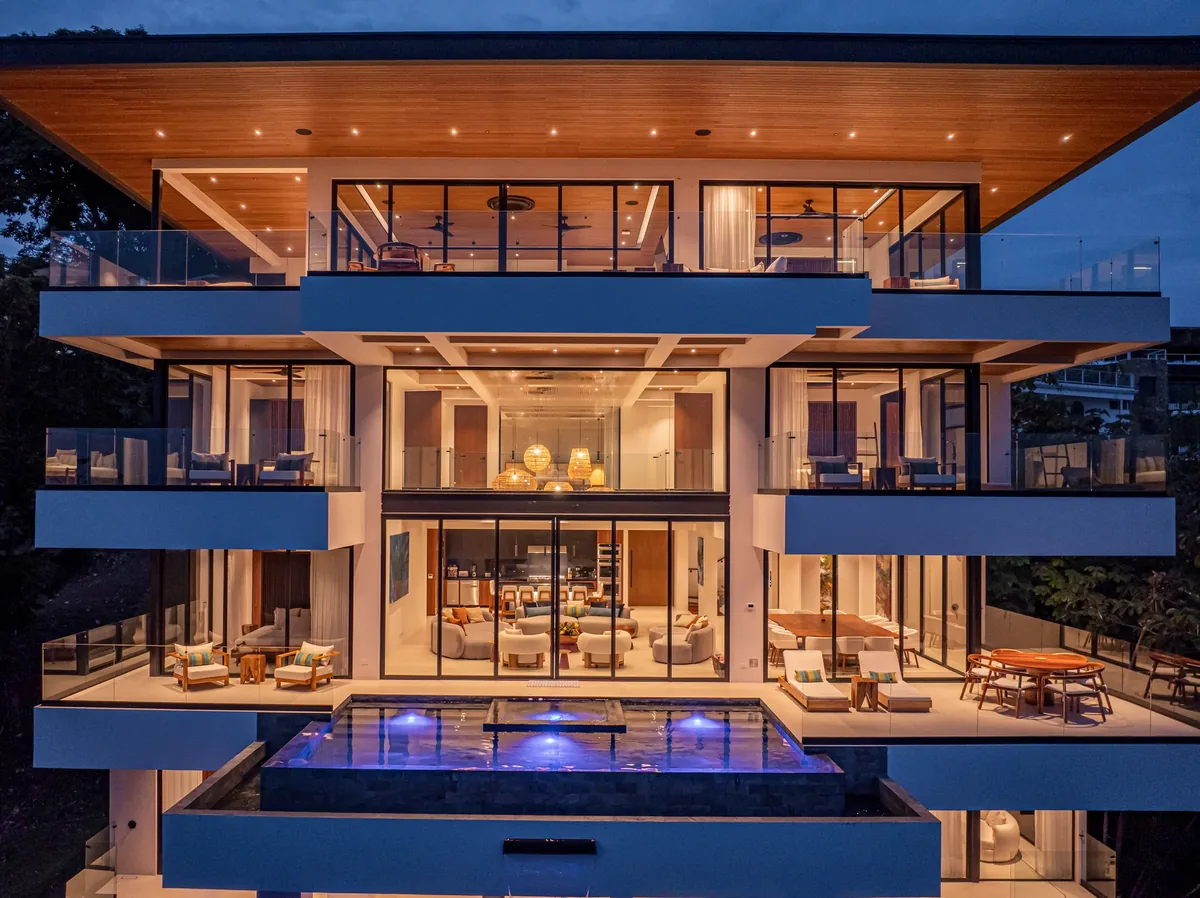 Alianz multi-level residence glowing warmly between rainforest trees at nightfall