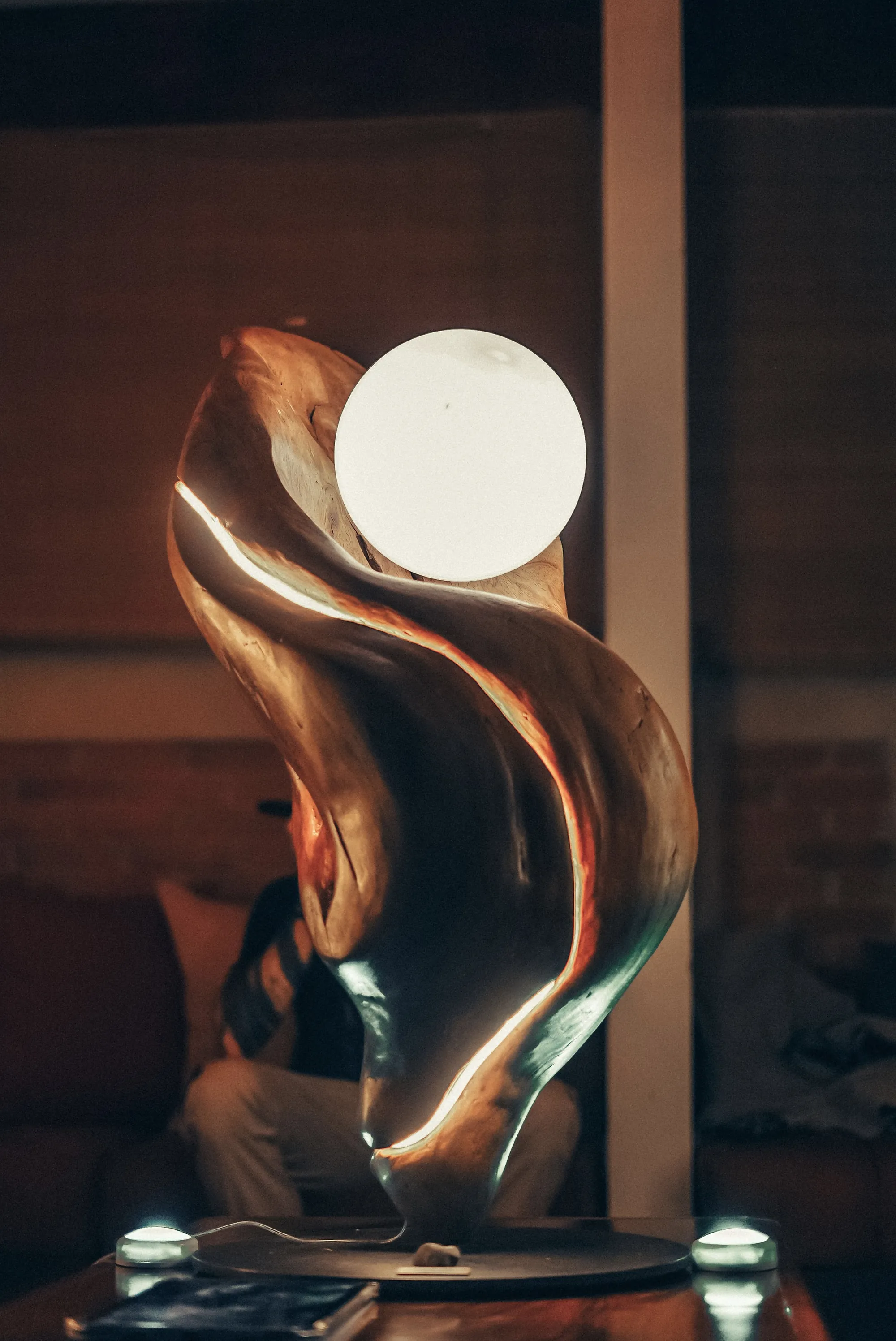 Brisa at night — a vertical sculpture crowned by a glowing sphere, a seam of light tracing its body